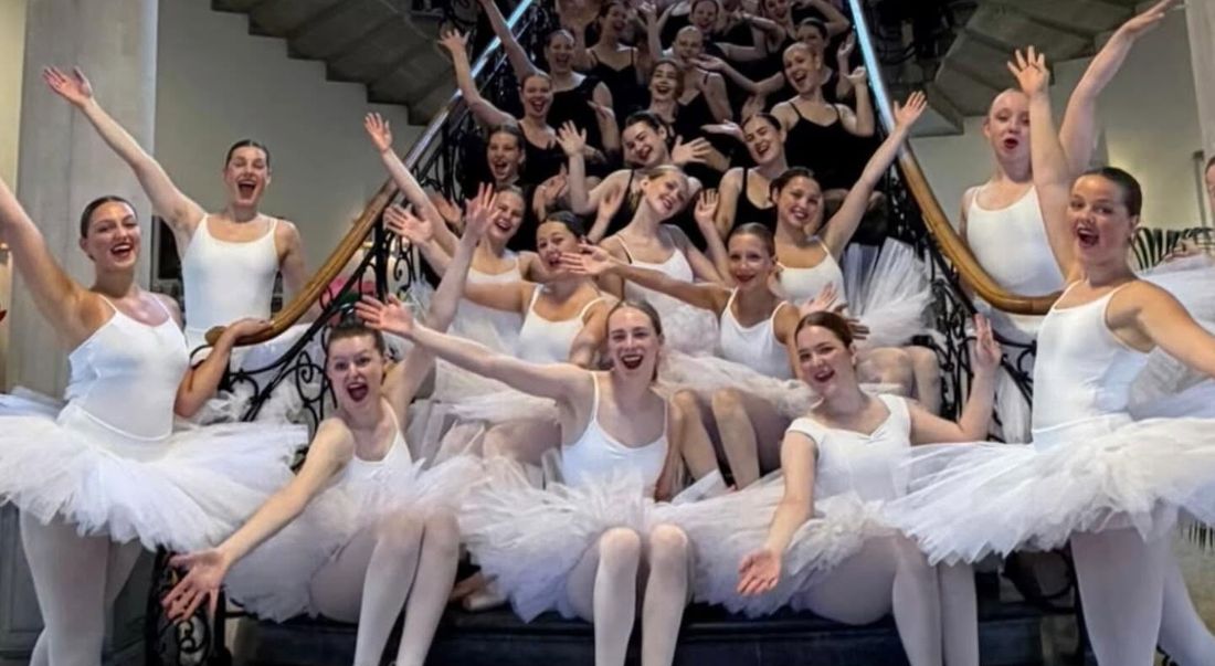 Groep jonge balletdansers in witte tutu's juicht met gestrekte armen op een trap