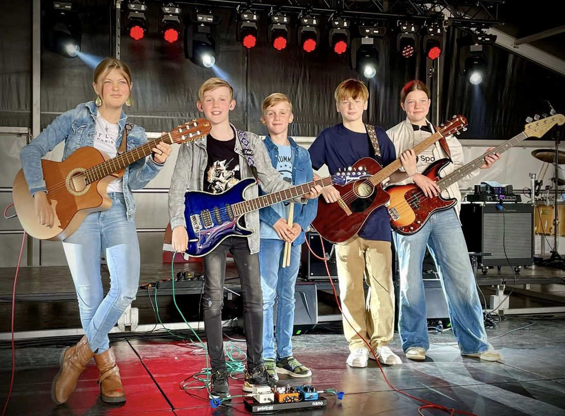 Vijf kinderen met gitaren poseren op een podium tijdens een muziekoptreden